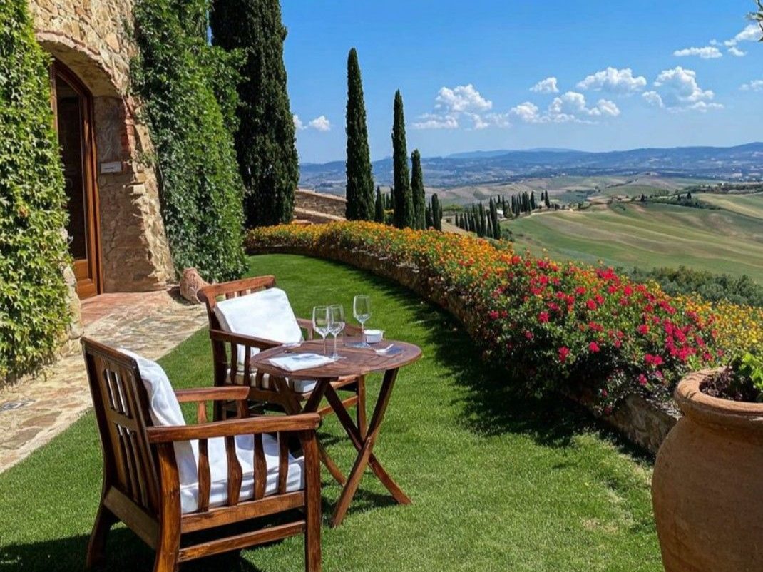Terrace of a Tuscan farmhouse with two chairs, wine glasses and the hills beyond